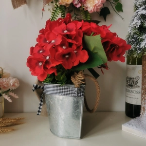 Detail of faux red geraniums in a rustic galvanized metal bucket with buffalo plaid bow