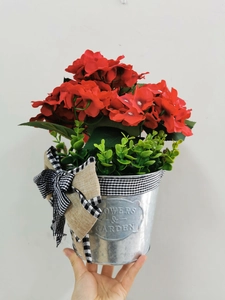 Detail of red geranium flowers in a rustic zinc bucket with a plaid bow decoration