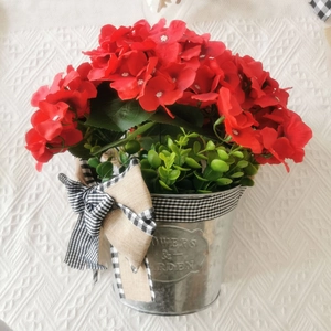 Detail of red faux geraniums in a silver metal flower pot with a plaid bow decoration