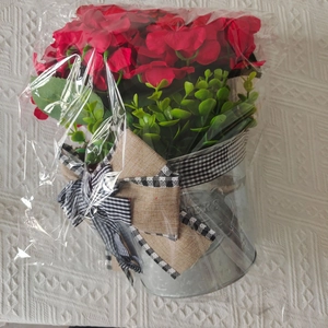 Detail of red artificial geraniums in a metal flower bucket with a decorative bow