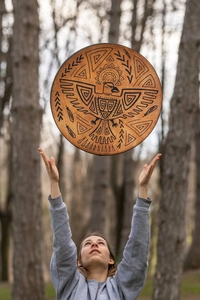 Action shot of a shamanic eagle drum being tossed in a serene forest setting