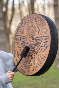 Outdoor close-up of a shamanic drum featuring a tribal eagle pattern and wooden drumstick