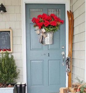 Christmas hanging basket with red geraniums and rustic bow on a light blue door