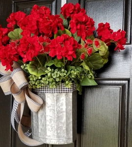 Detail of red geraniums in a vintage galvanized bucket with a plaid burlap bow decoration