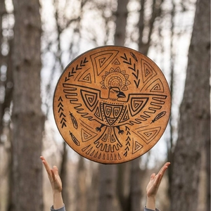 Ethnic shaman drum featuring black eagle totem and patterns against forest background