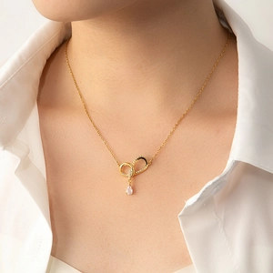 Detail of gold heart and infinity necklace with zircon teardrop pendant on model
