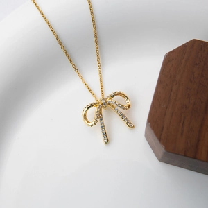 Close-up of golden bow pendant with pavé zircon stones on white ceramic and walnut background