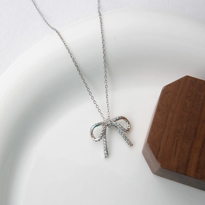Elegant silver bow pendant necklace with zircon stones on a white ceramic plate