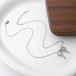 Macro view of silver bow pendant with zircons and lobster clasp on white ceramic