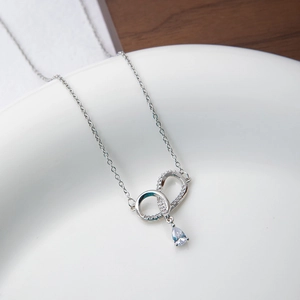 Detail of silver dual-interlocking rings pendant with pear-shaped zircon on a porcelain plate