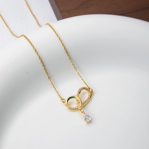 Detailed close-up of golden infinity necklace with dangling drop zircon on a white tray