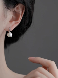 Gros plan d'une perle ronde blanche avec fermoir en métal argenté portée sur l'oreille