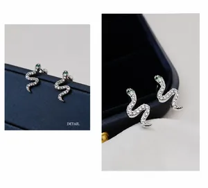 Macro view of silver snake stud earrings with pavé white zircons and green gem eyes