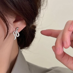 Sparkling silver snake-shaped stud earrings set with zircons on an ear model
