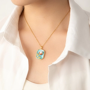 Détail d'un pendentif fleur émaillé avec perle sur chaîne dorée porté par un mannequin