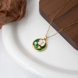 Détail du collier avec pendentif en émail floral et perles blanches sur plat en céramique