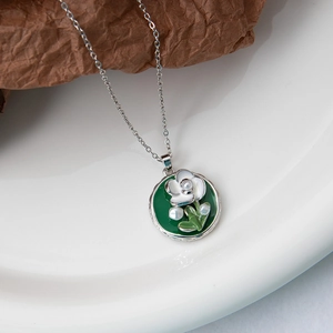 Gros plan du pendentif fleur en émail argenté avec perles sur une assiette décorative