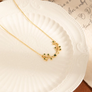 Élégant collier branche d'olivier dorée avec gemmes émeraudes sur assiette blanche