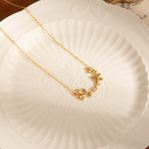 Détail d'un collier branche d'olivier dorée avec zircons sur de la céramique blanche