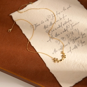 Élégant collier branche d'olivier dorée avec pierres noires sur fond papier vintage