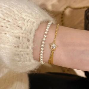 Detail of star zircon bracelet and pearl chain worn on white knit sweater sleeve