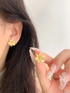 Detailed macro view of matte gold lily flower earrings with textured petals on ear