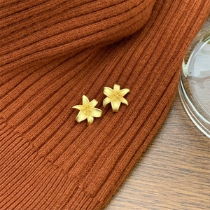 Matte gold lily flower stud earrings with a brushed texture on a brown knit background