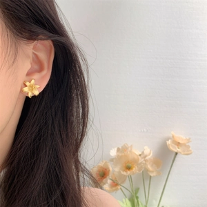 Close-up of matte gold lily flower stud earring worn by model in a soft lighting