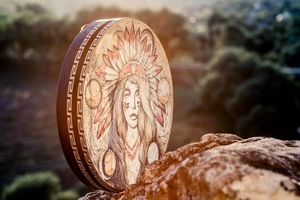 Detail of handmade Shaman drum with colorful feather crown illustration on forest rocks