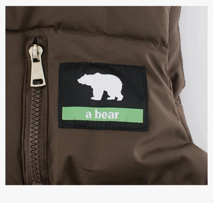 Close-up of brown quilted vest featuring a bear patch and premium gold metal zipper