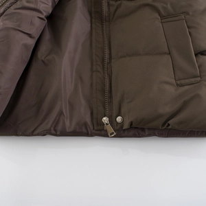 Detail of dark brown quilted vest featuring a resin zipper and metal snap button bottom