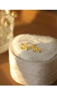 Macro view of gold four-leaf flower studs with matte finish and center zircon detail