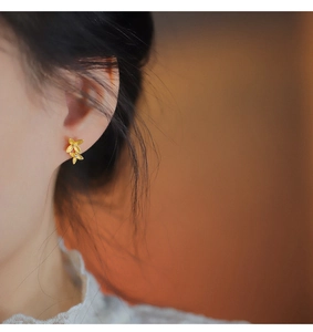 Detail of matte gold four-leaf flower earrings with diamonds on a model ear