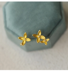 Macro view of matte gold four-petal flower studs with center diamond on green velvet box