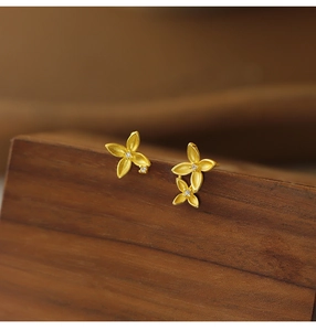 Detailed close-up of gold matte flower earrings with micro-inlaid stones on wooden stand