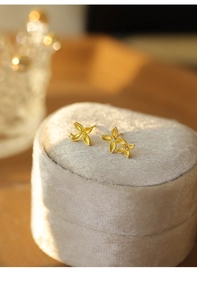 Macro shot of asymmetric gold flower earrings with brushed texture and zircon crystals