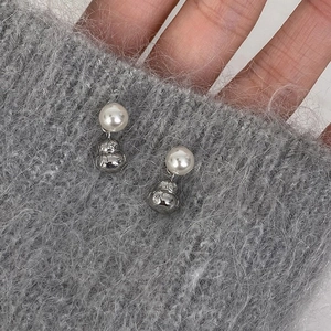 Macro view of pearl earrings with silver gourd pendants on grey knitted texture