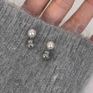 Macro shot of pearl stud earrings with silver money bag charms on knit fabric