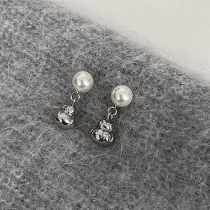 Macro detail of gourd-shaped silver pearl earrings on a soft grey textured fabric background