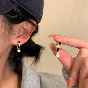 Détail de boucles d'oreilles étoile dorées avec émail noir et pierre de zircon blanc