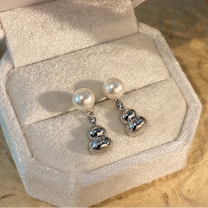 Macro detail of silver gourd pearl earrings in a velvet jewelry box with 925 engraving