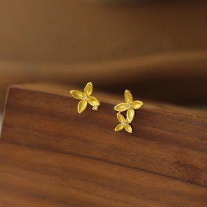 Matte gold clover earrings with rhinestones on a dark wood background in a 45-degree angle