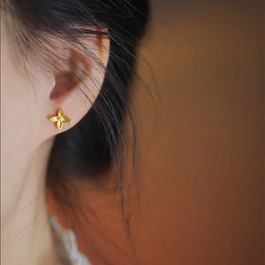 Elegant gold four-leaf flower stud earrings with shimmering micro-pave diamonds on model