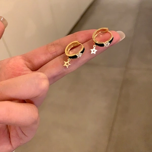 Détail de boucles d'oreilles dorées en émail noir avec pendentifs étoiles tenues en main