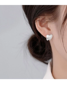 Macro view of matte silver heart stud earrings with star engraving on model