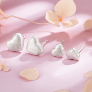Macro shot of two pairs of brushed metal heart stud earrings on a soft pastel background