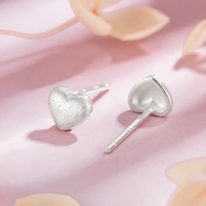 Macro shot of brushed heart stud earrings with S925 engraving on a pink floral background