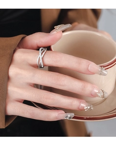 Close-up of a silver X-shaped layered ring with pavé-set zircons worn by a person