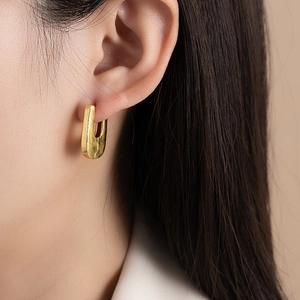 Minimalist matte brushed gold U-shaped earrings displayed on a model earlobe