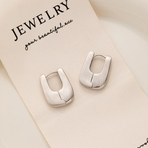 Detail of silver U-shaped earrings with brushed matte finish on a minimalist display card